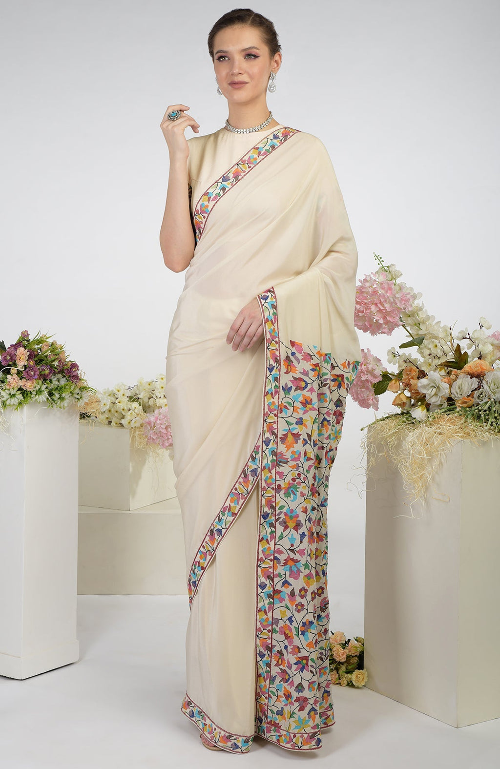 A woman models a butter cream pure crepe silk saree with colorful Kani art embroidery.