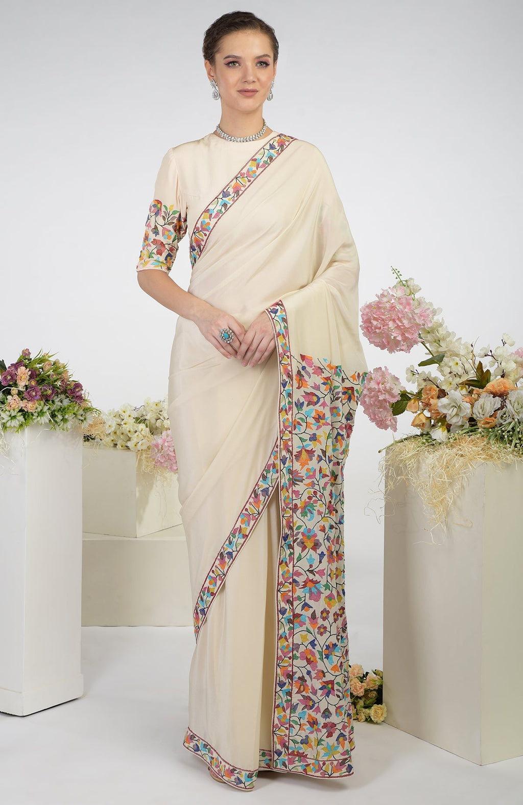 A woman models a butter cream pure crepe silk saree with colorful Kani art embroidery.
