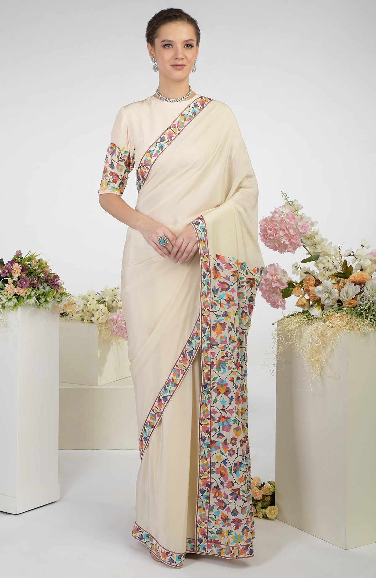 A woman models a butter cream pure crepe silk saree with colorful Kani art embroidery.