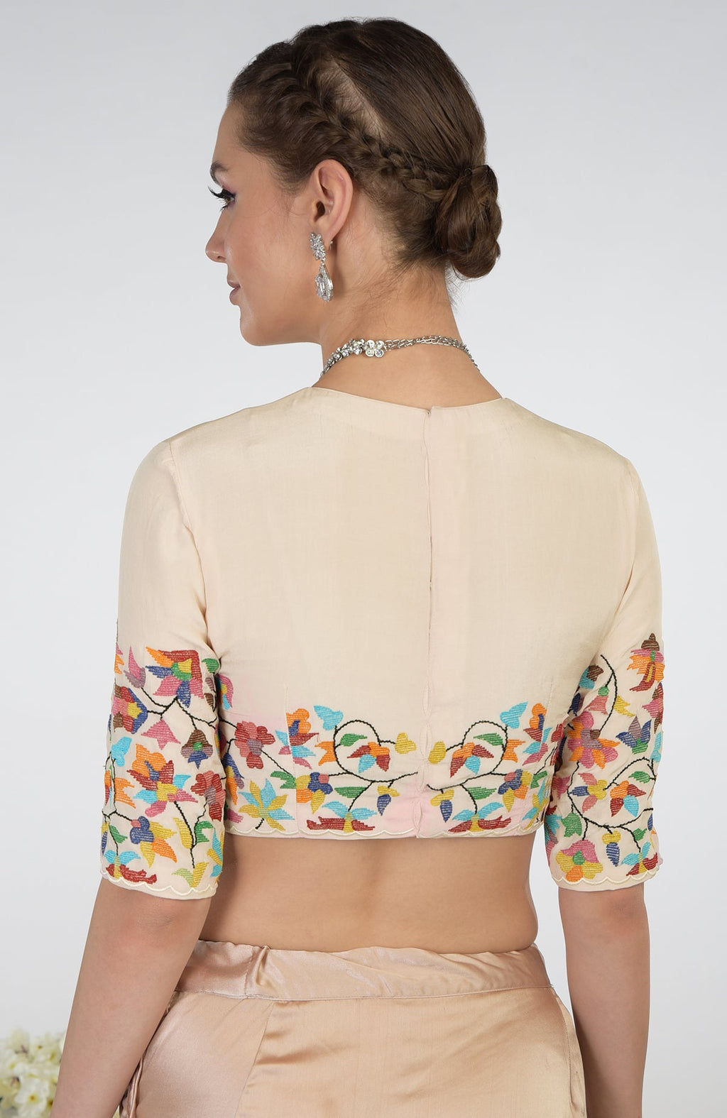 A woman models a butter cream pure crepe silk blouse with colorful floral embroidery.