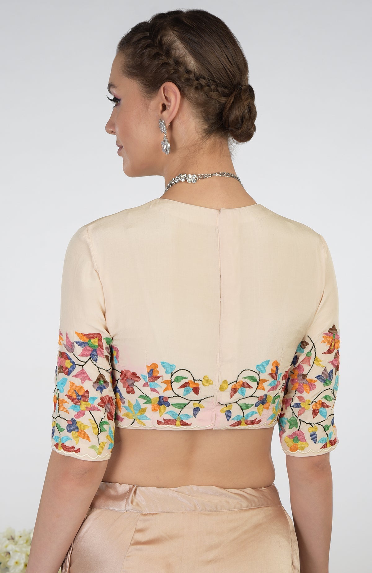 A woman models a butter cream pure crepe silk blouse with colorful floral embroidery.
