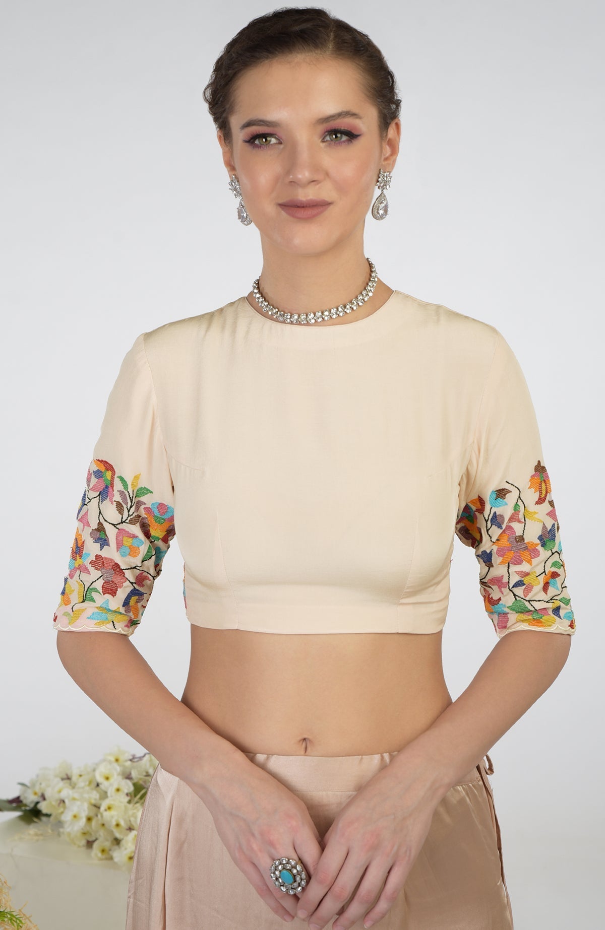 A woman models a butter cream pure crepe silk blouse with colorful floral embroidery on the sleeves.