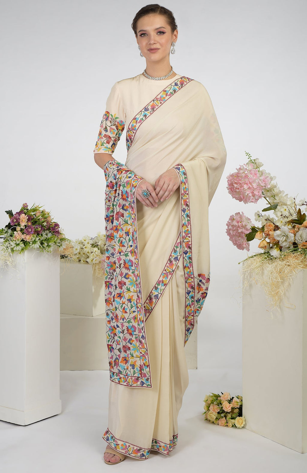 A woman models a butter cream pure crepe silk saree with colorful floral embroidery.