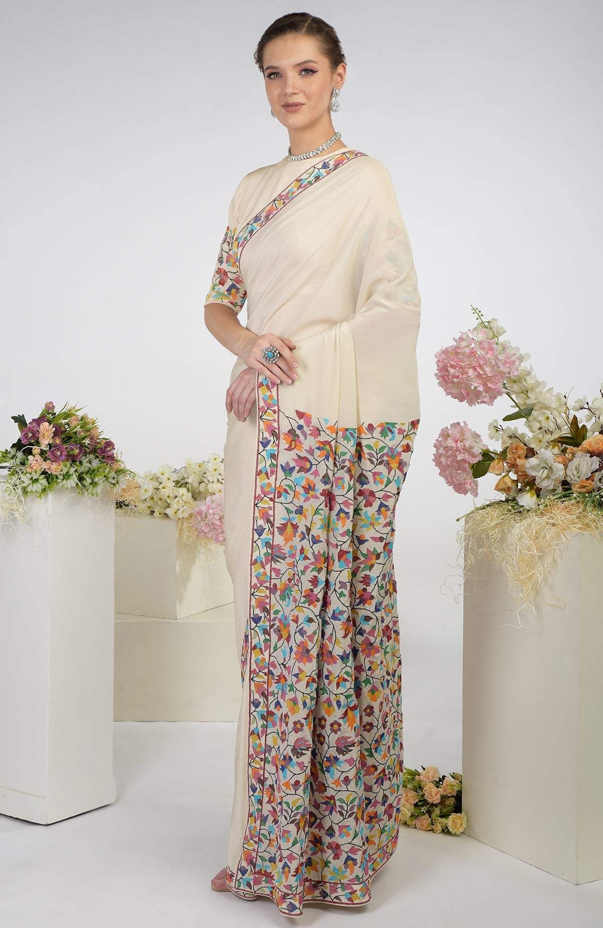 A woman models a butter cream pure crepe silk saree with colorful floral embroidery.