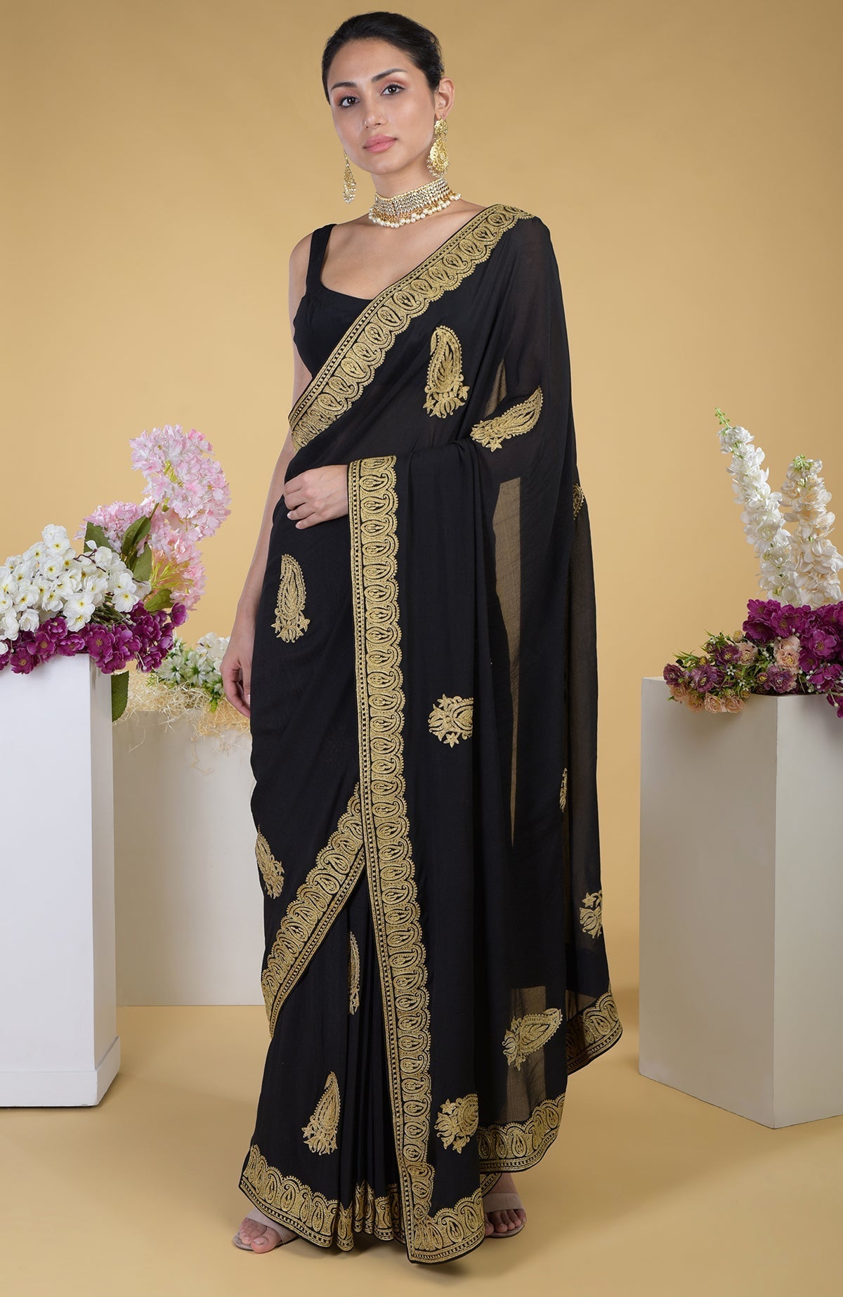 A woman models a black saree with gold paisley embroidery and a matching blouse.