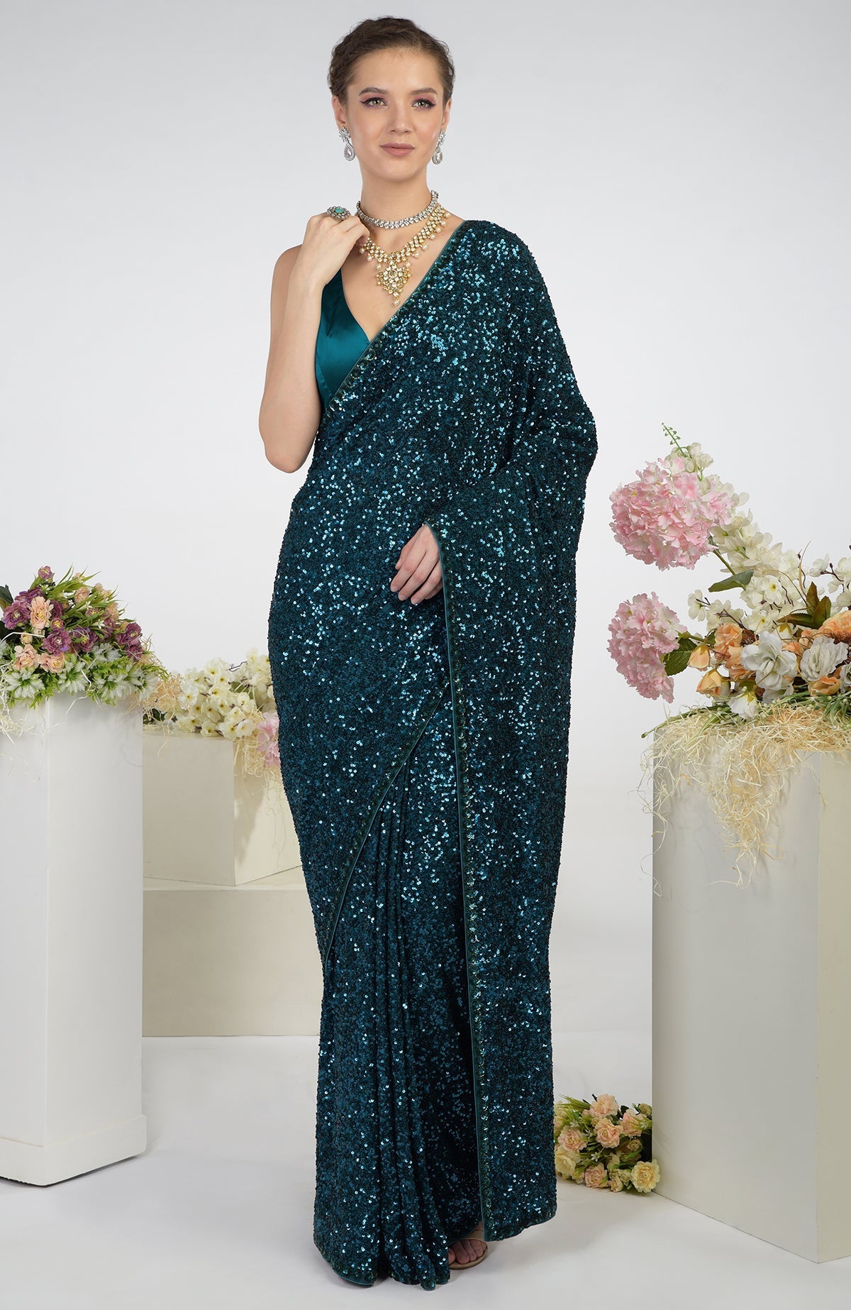 Woman in a teal sequin saree with a matching blouse and gold jewelry.