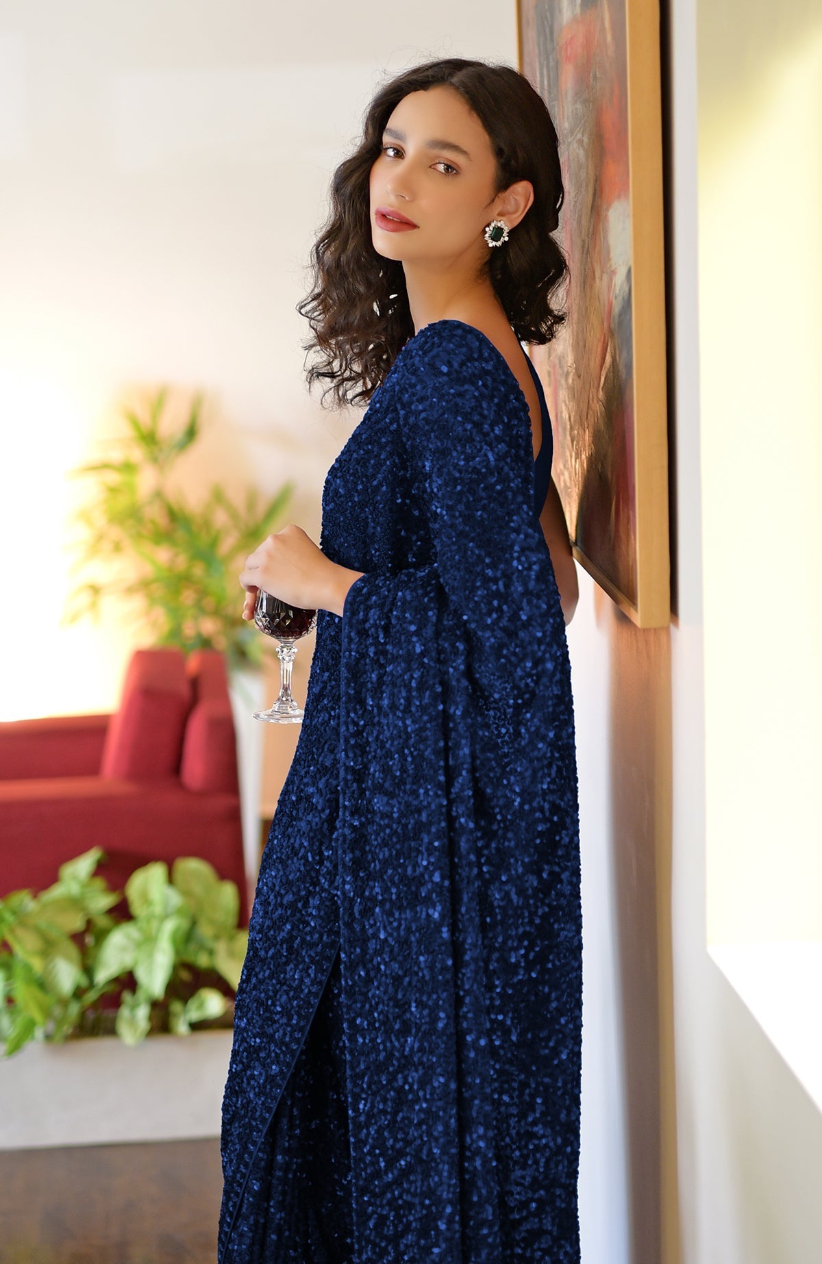A woman in a sapphire blue sequin saree holds a glass of red wine.