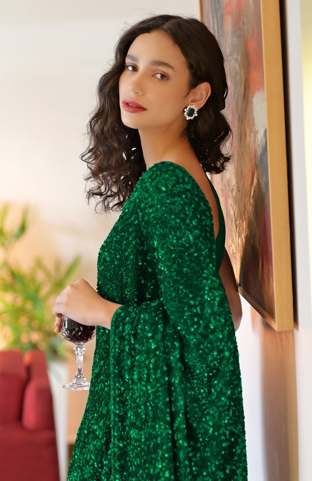 Woman in an emerald green sequin saree holding a glass of red wine.