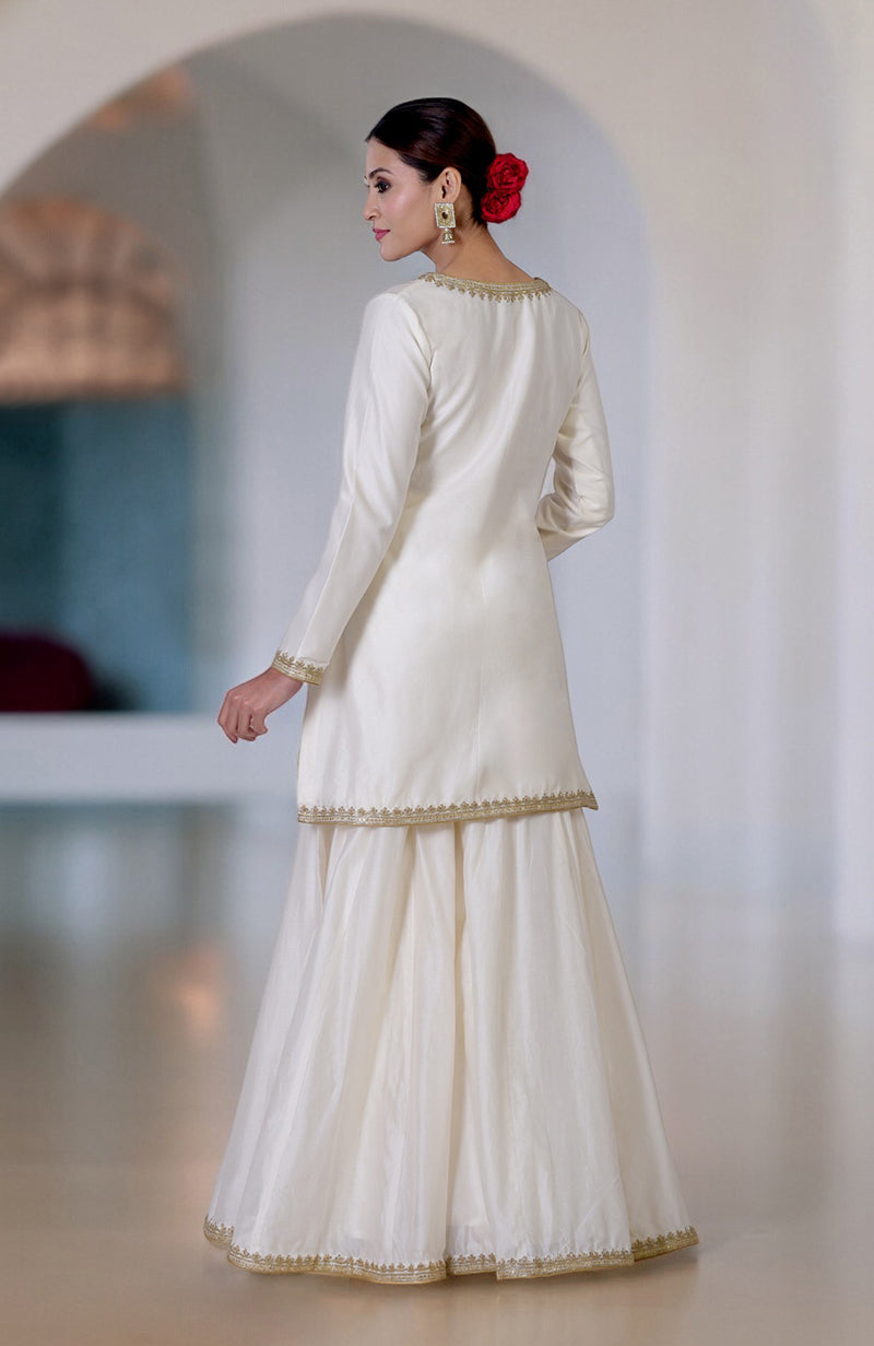 An elegant ivory sharara set with gold embroidery, worn by a woman with a red rose in her hair.