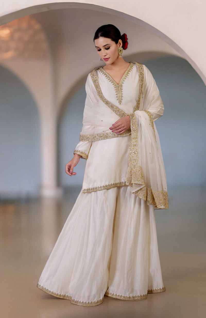 An ivory sharara set with gold marori and zardozi hand embroidery.