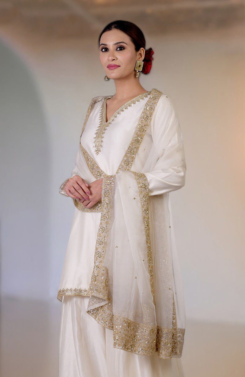 An ivory sharara set with gold marori and zardozi hand embroidery.
