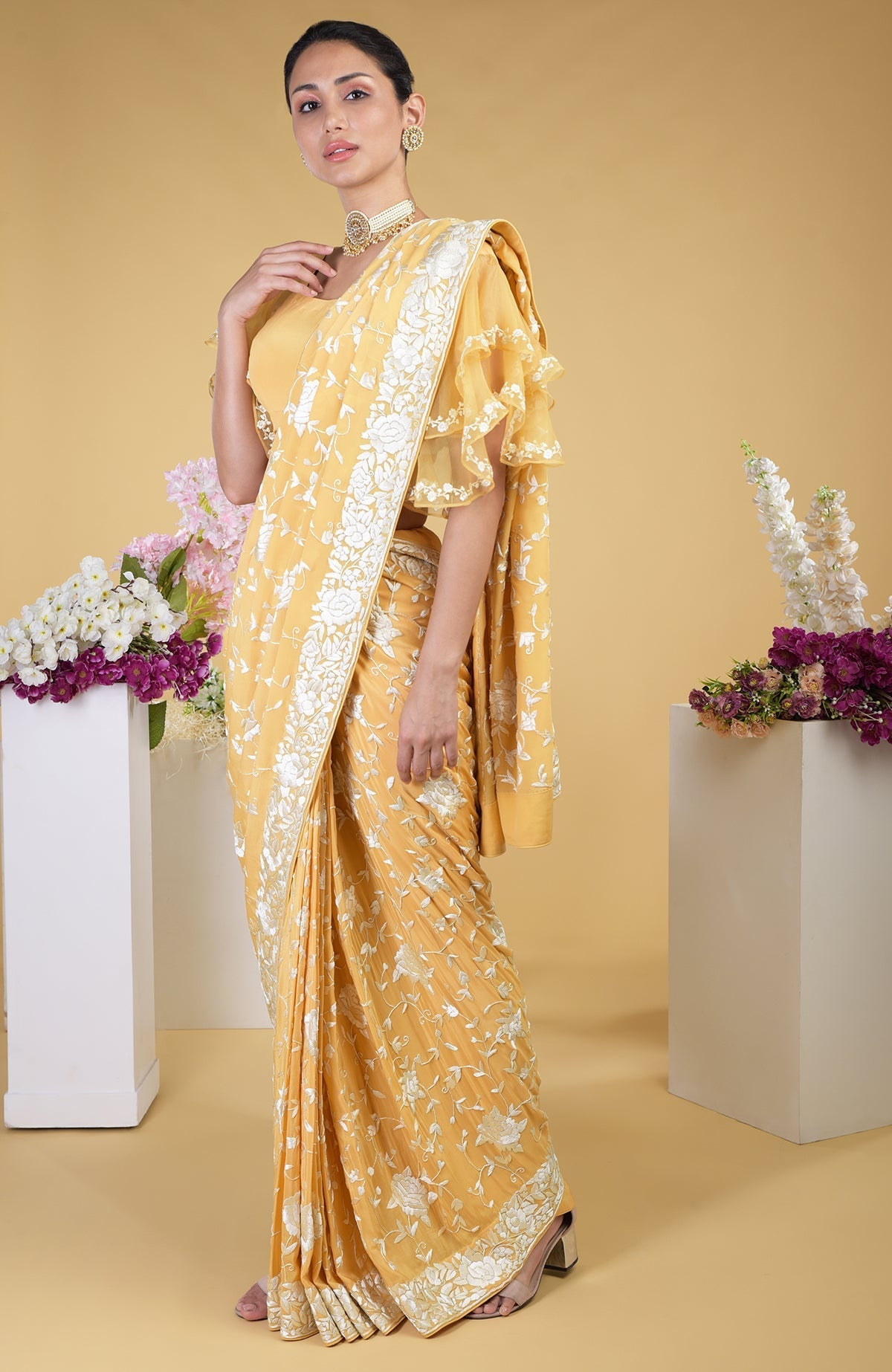 A woman models a mango yellow Parsi Gara hand-embroidered saree with a frill blouse.