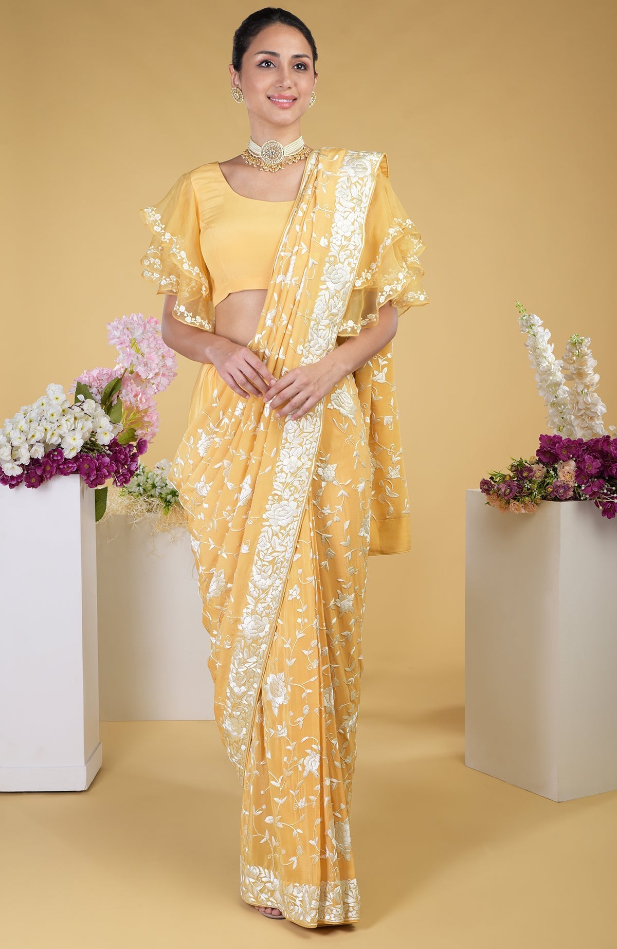 A woman models a mango yellow Parsi Gara hand-embroidered saree with a matching blouse.