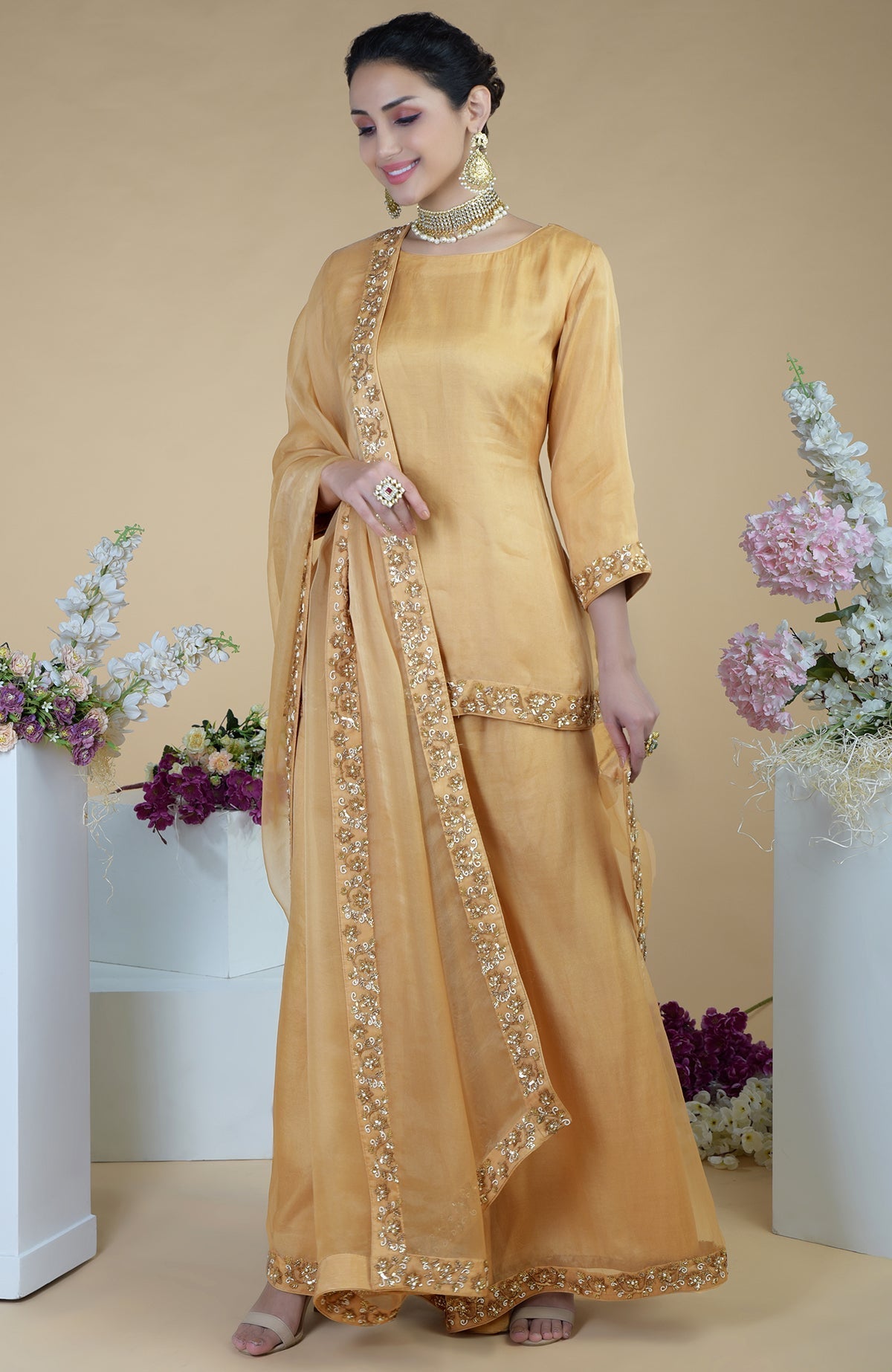A woman models a gold zardozi hand-embroidered sharara set with a matching dupatta.