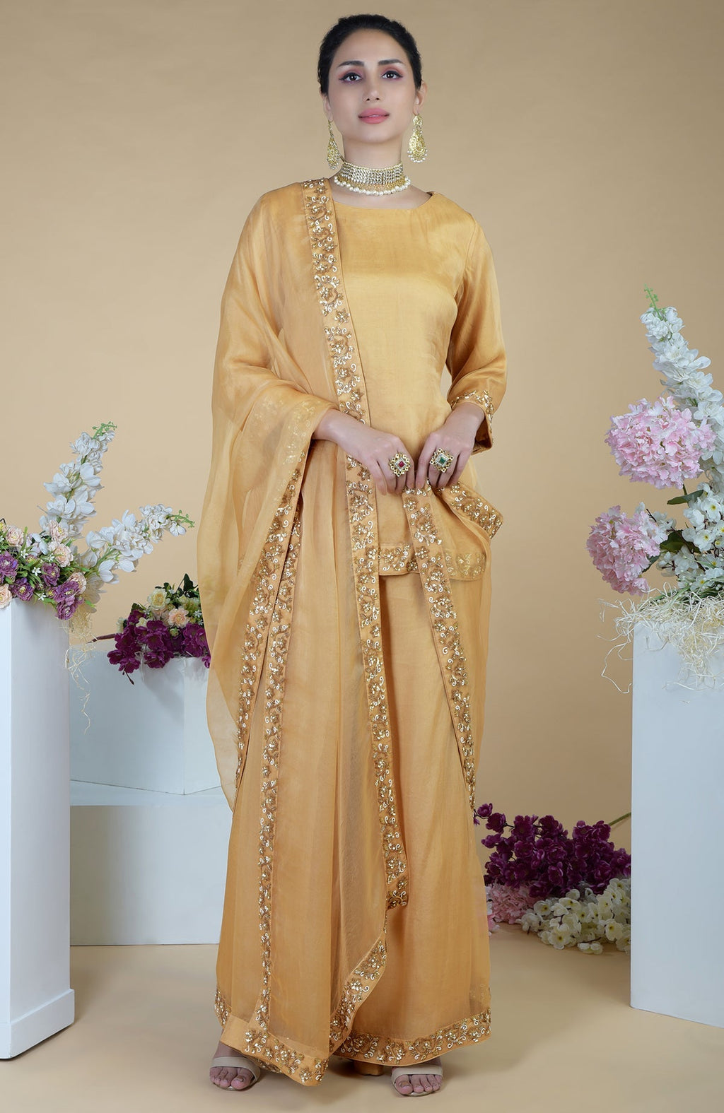 A woman models a gold zardozi hand-embroidered sharara set with a matching dupatta.