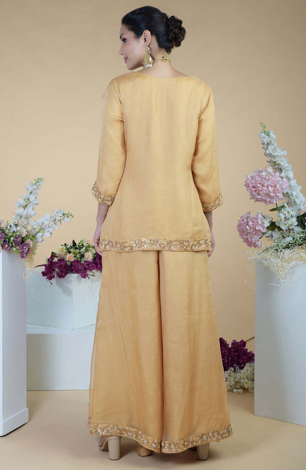 A woman models a gold zardozi hand-embroidered sharara set with floral details.
