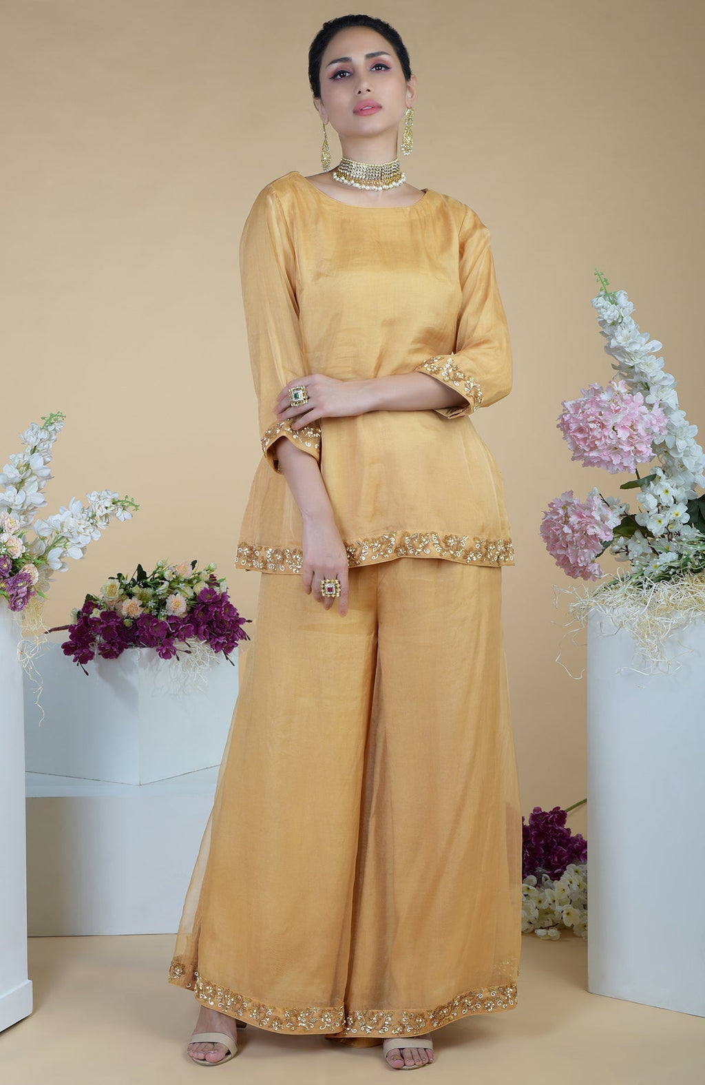 A woman models a gold zardozi hand-embroidered sharara set with matching jewelry.