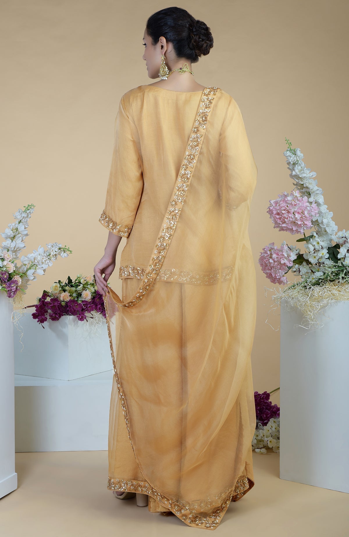 A woman from behind wears a gold zardozi hand-embroidered sharara set.