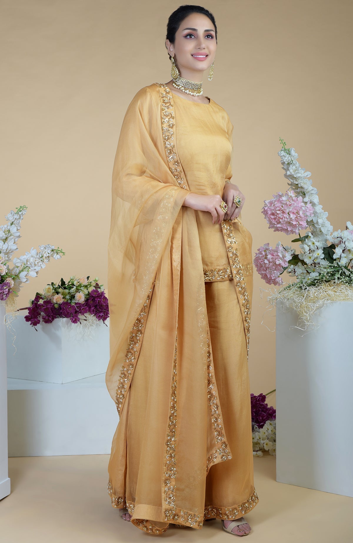 A woman models a gold zardozi hand-embroidered sharara set with a matching dupatta.