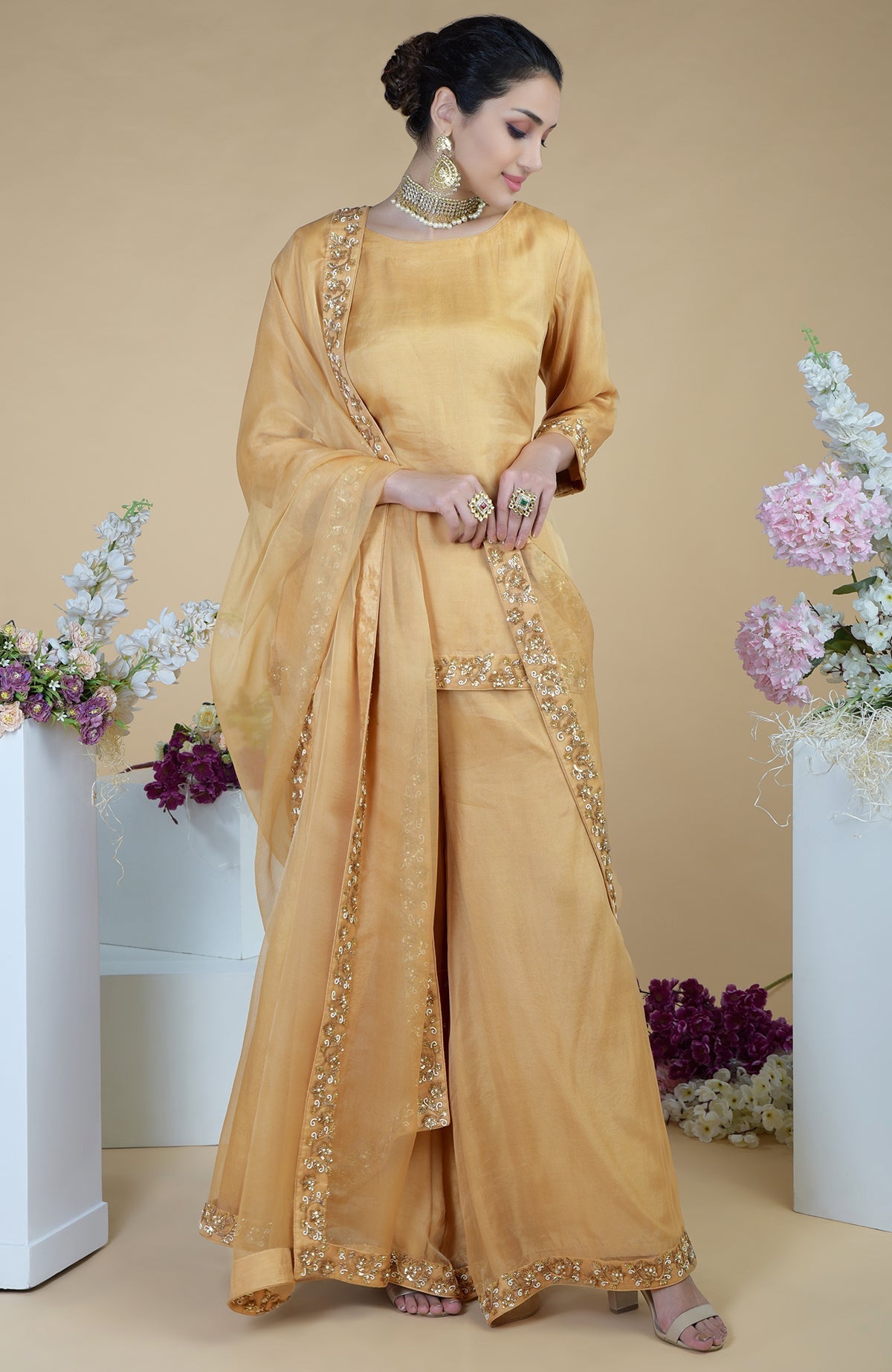 A woman models a gold zardozi hand-embroidered sharara set with a matching dupatta.