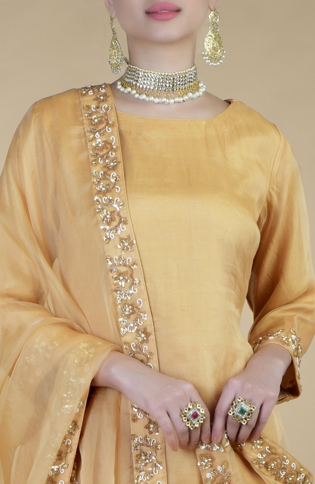 A woman models a gold zardozi hand-embroidered sharara set with jewelry.