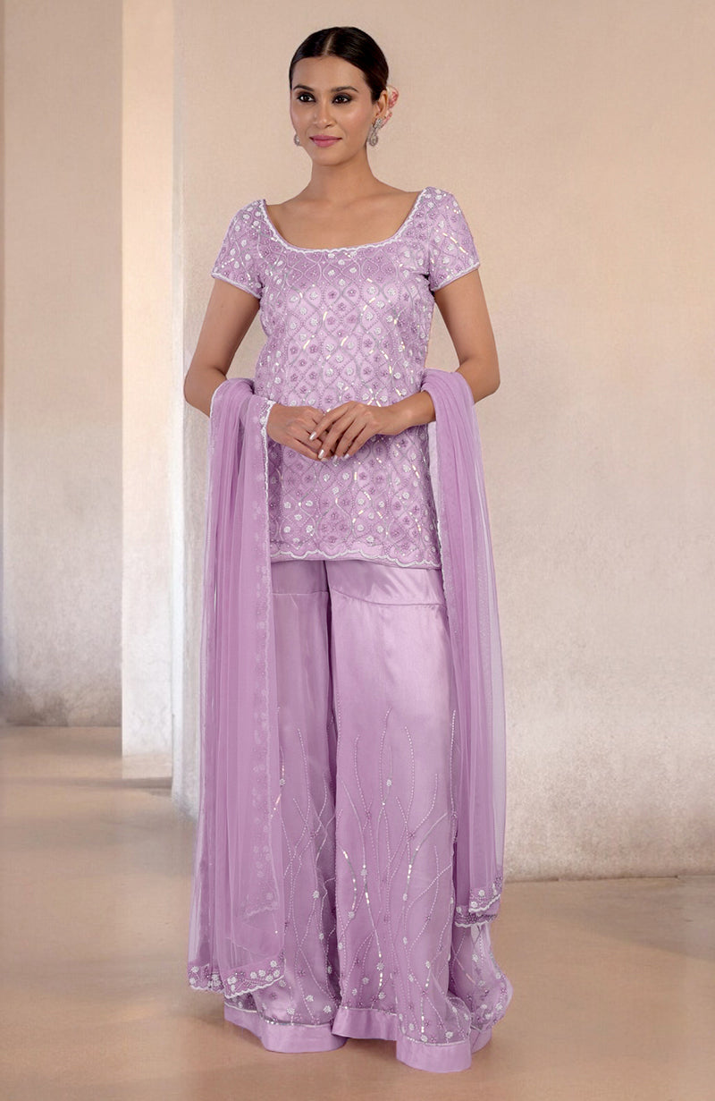 A woman models a lilac silk organza hand-beaded sharara set with a matching dupatta.
