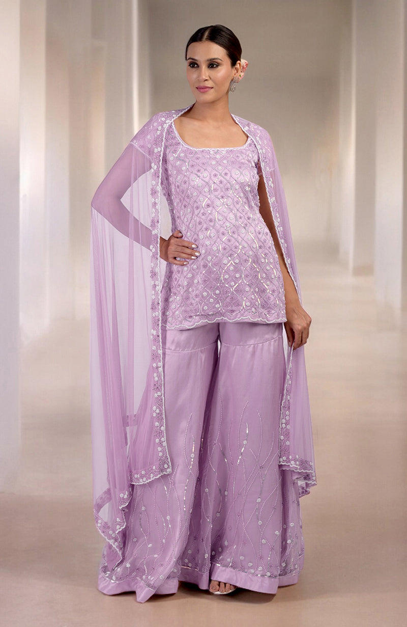 A woman models a lilac silk organza hand-beaded sharara set with a sheer cape.