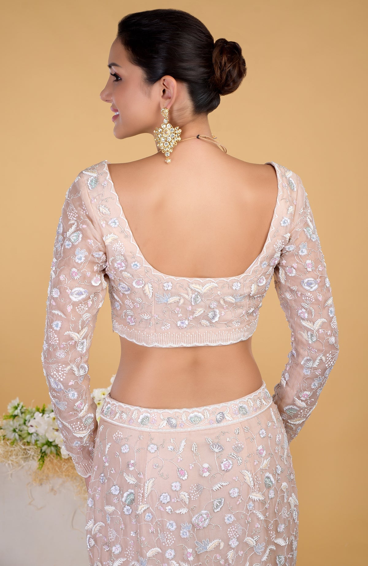 A woman models a light pink embroidered blouse and skirt from the back.