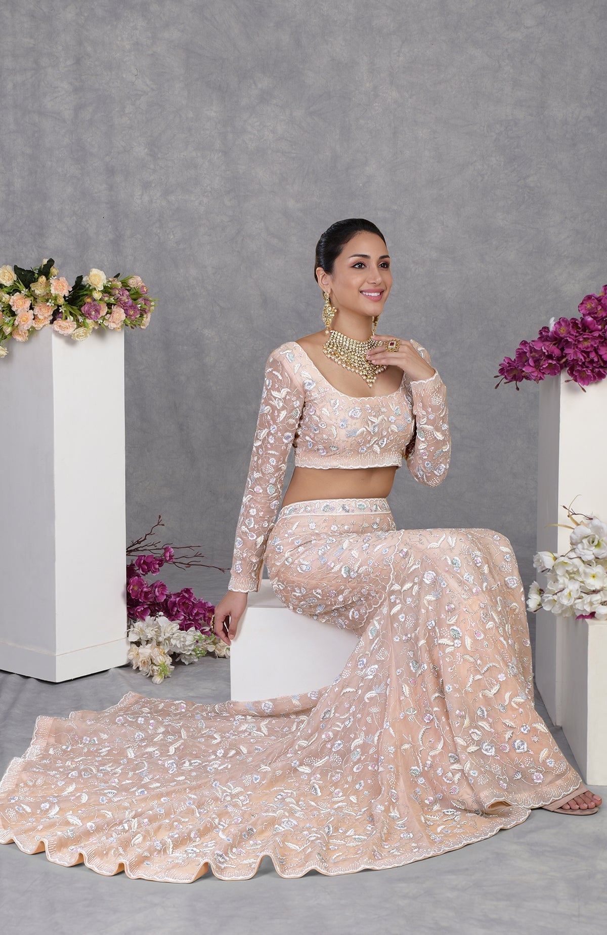 A woman in a peach embroidered crop top and matching skirt with a long train.