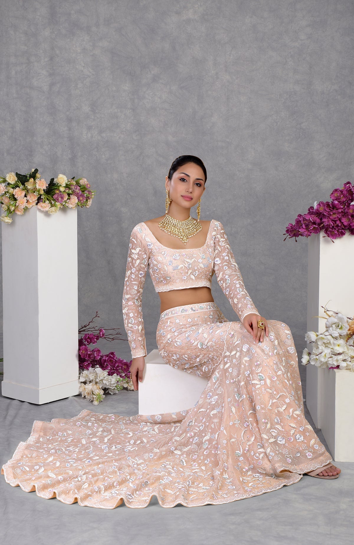 A woman models a peach embroidered crop top and matching skirt with a long train.