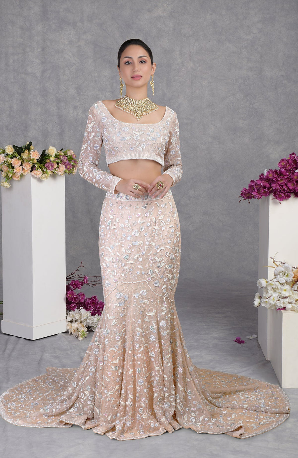 A woman models a light peach embroidered crop top and matching mermaid-style skirt with a train.