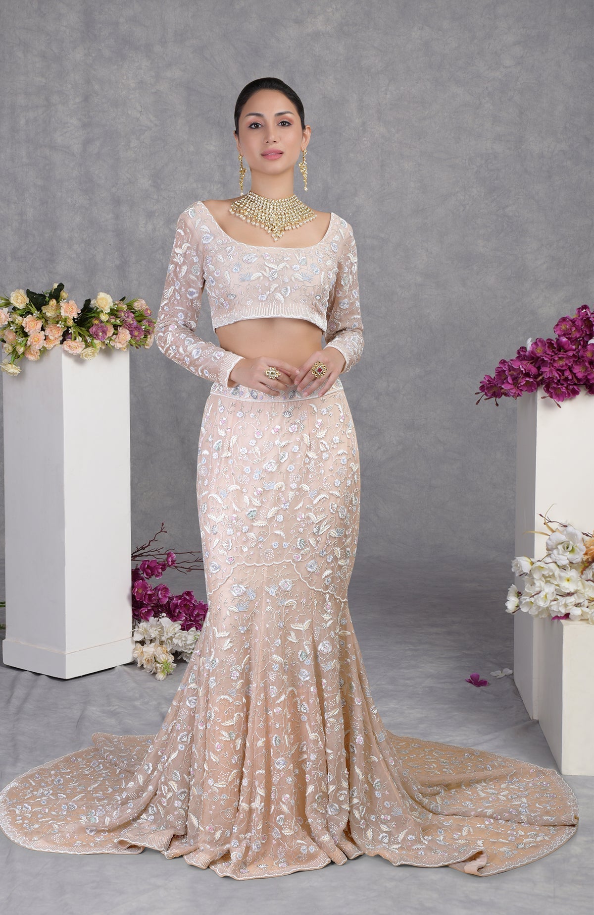 A woman models a light peach embroidered crop top and matching mermaid-style skirt with a train.