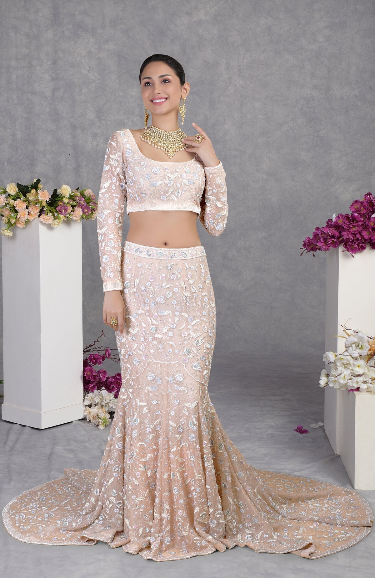 A woman models a light pink embroidered crop top and matching mermaid-style skirt with a train.