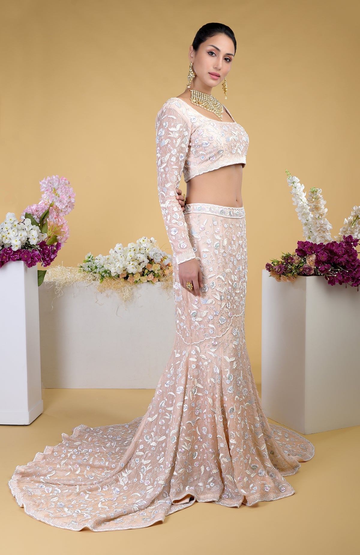 A woman models a peach embroidered crop top and matching mermaid skirt with a long train.