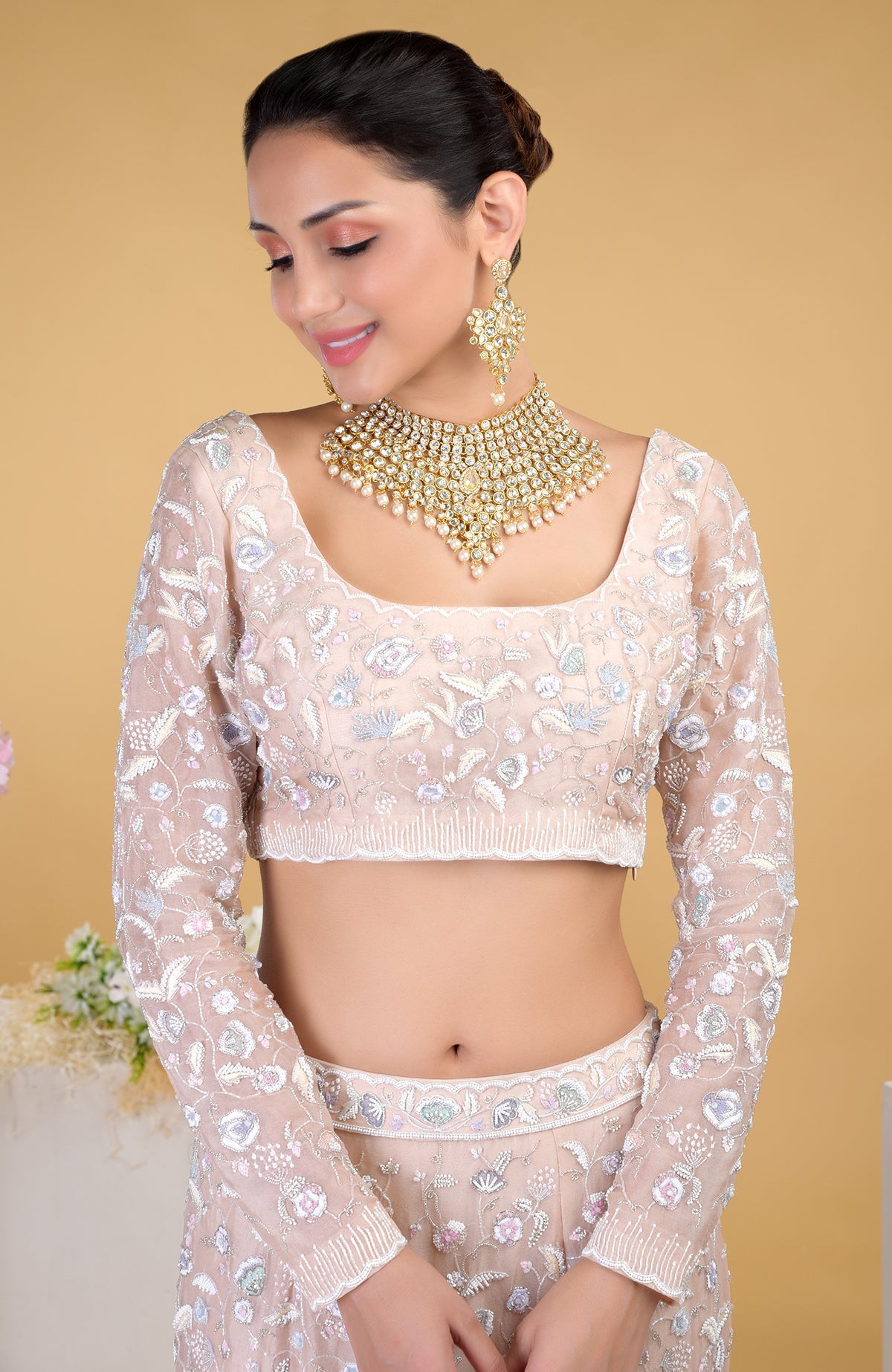 A woman models a light pink embroidered lehenga set with a matching necklace and earrings.