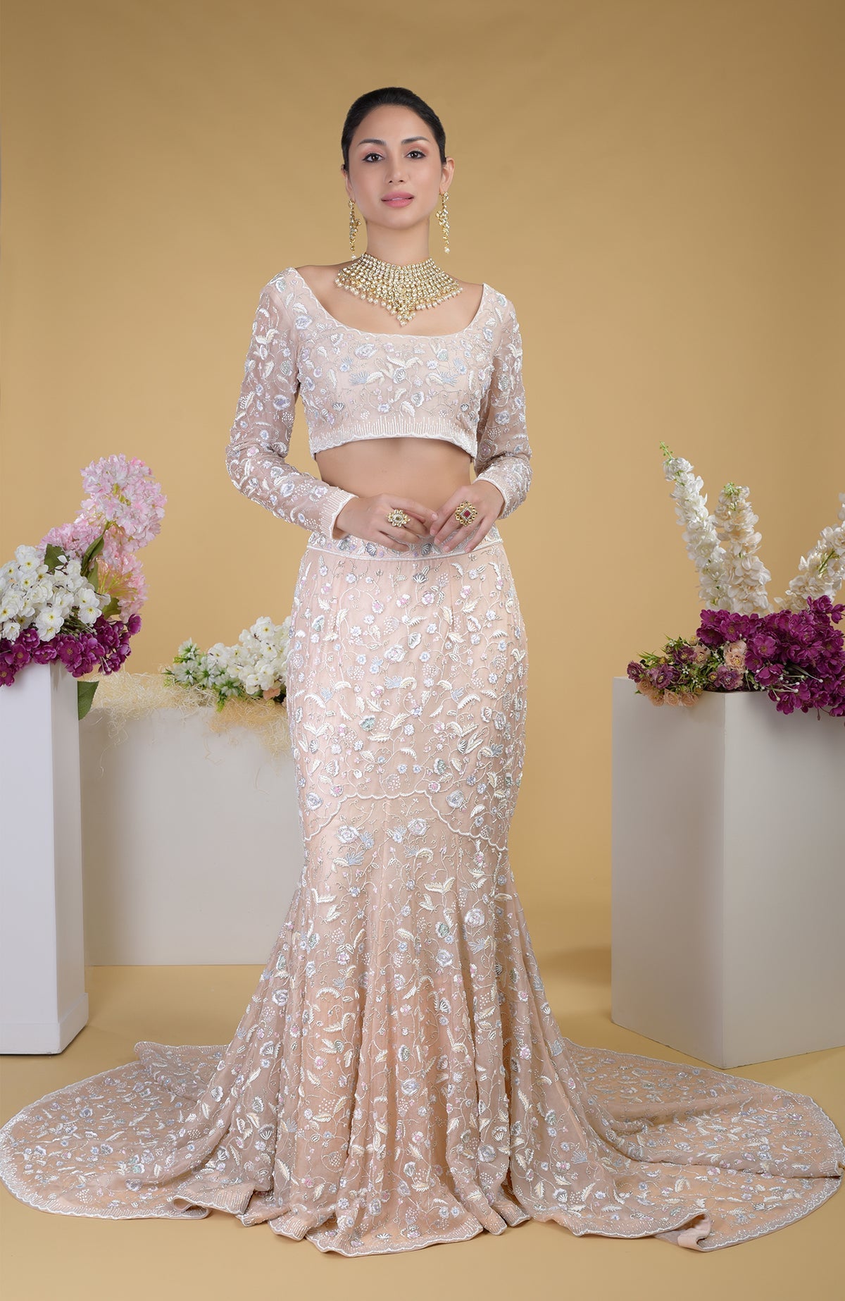 A woman models a light peach embroidered crop top and matching mermaid-style skirt with a train.
