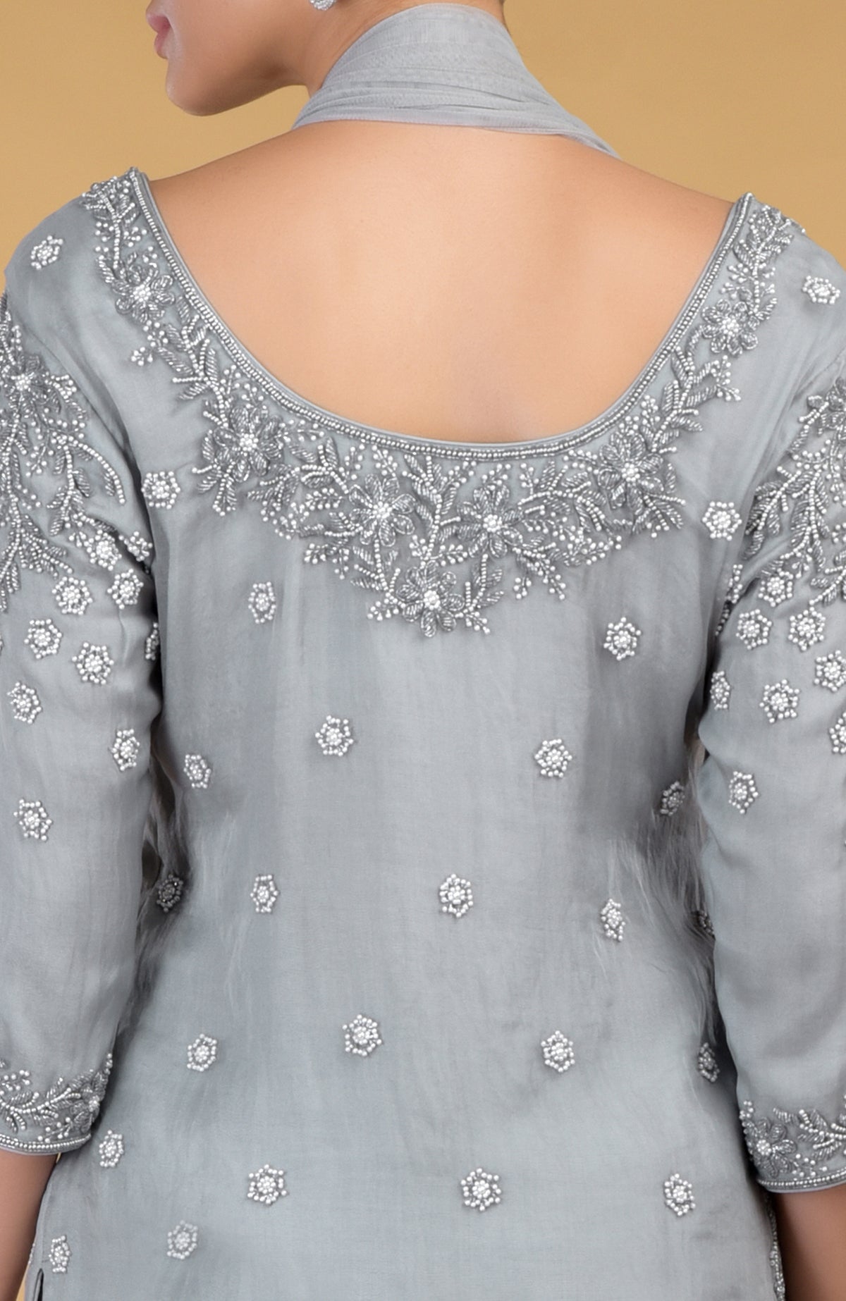A woman models the back of a grey silk organza kurta with intricate pearl embroidery.