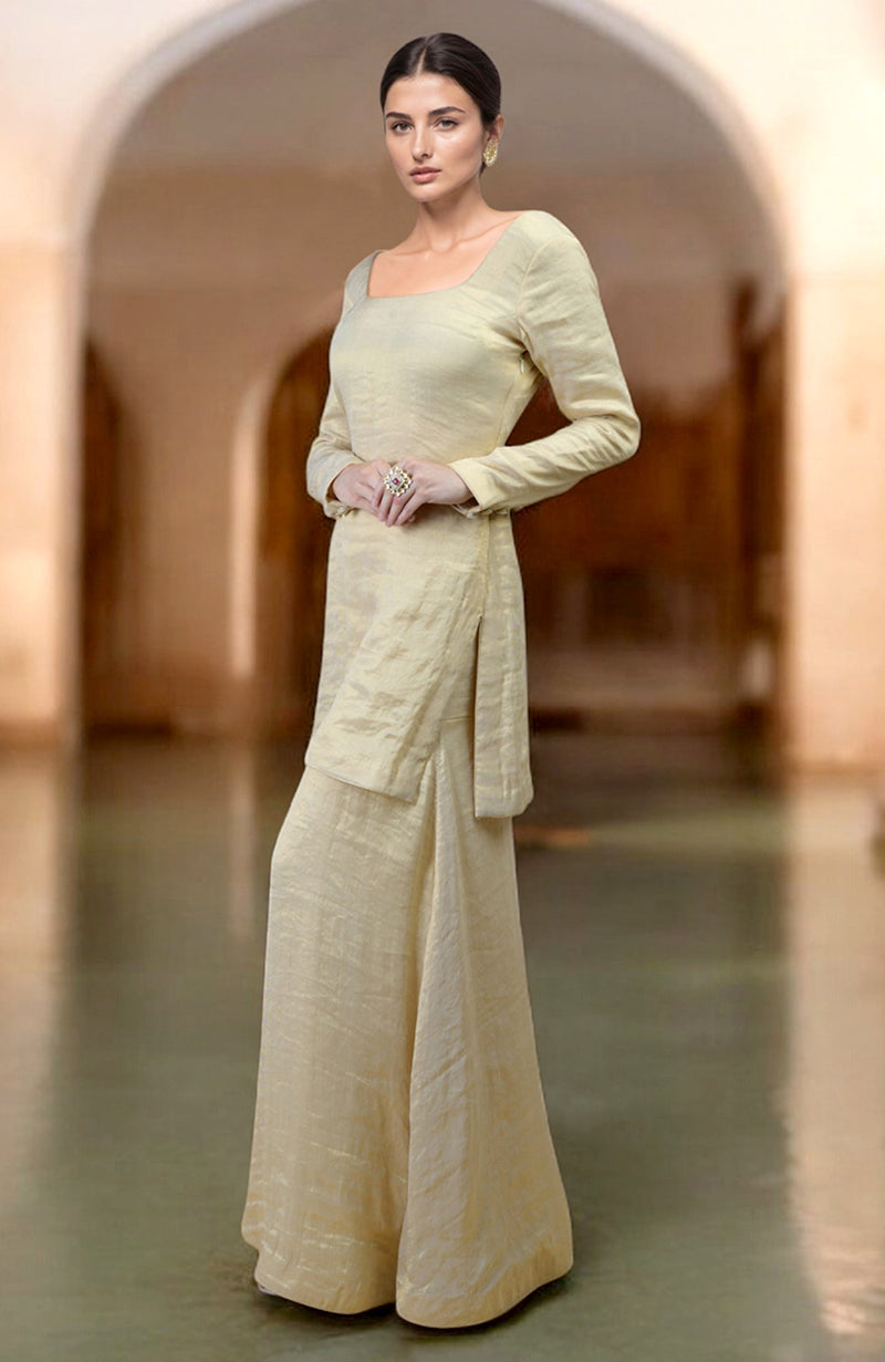 A woman models a gold tissue sharara suit with a short kurta and wide-leg pants.
