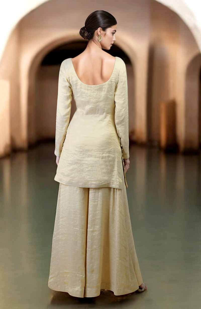 A woman in a gold tissue sharara suit with a scoop neck and long sleeves.