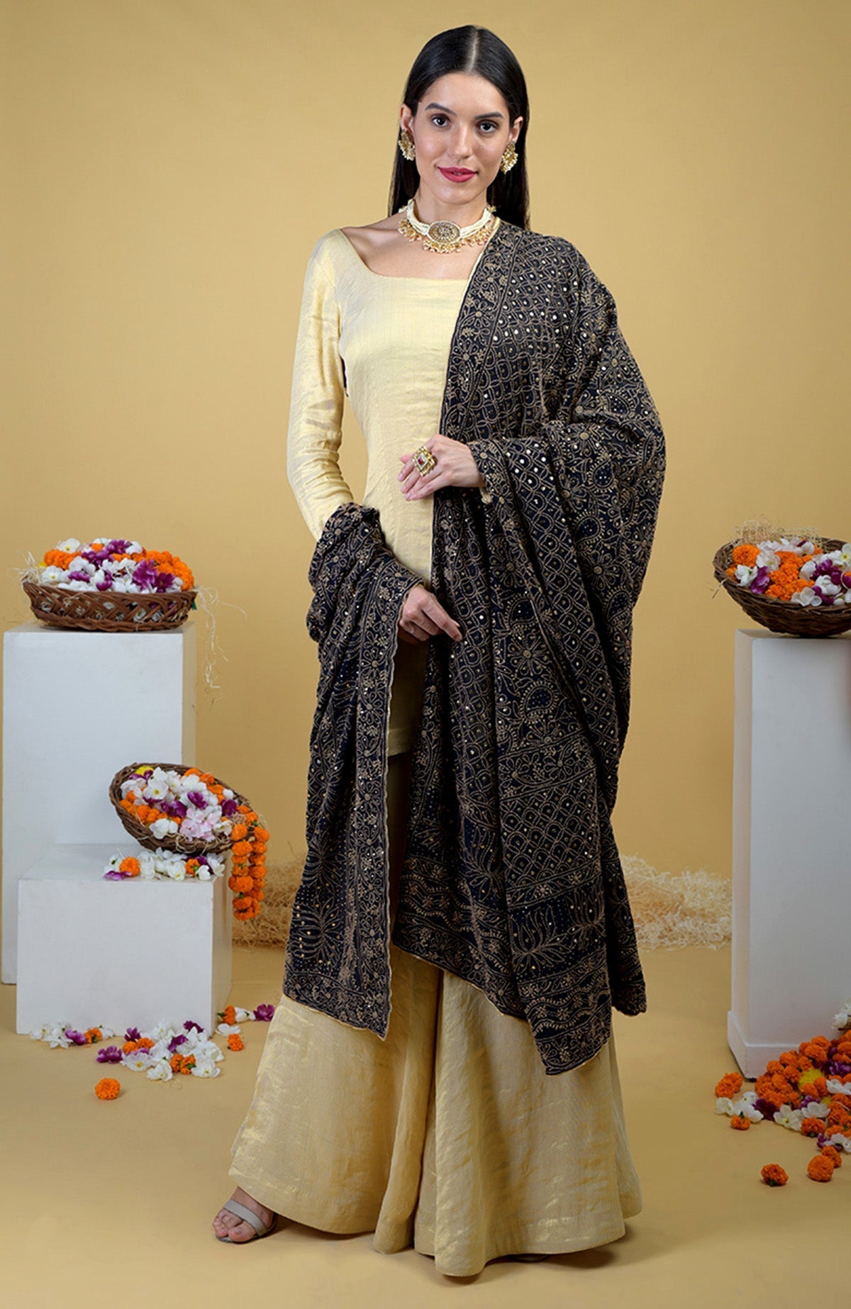 A woman in a gold tissue sharara suit with a black chikankari and kamdani dupatta.