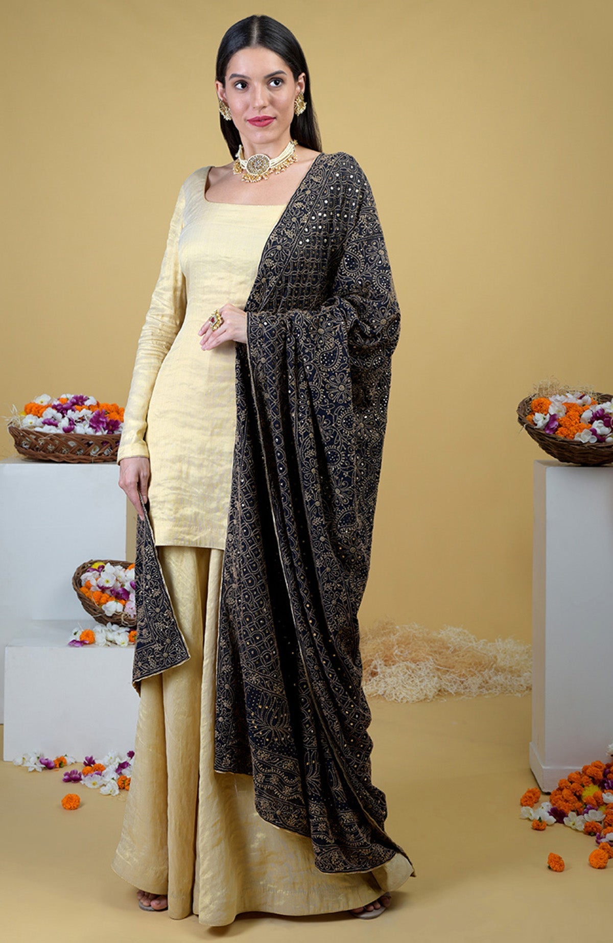 A woman in a gold tissue sharara suit with a black chikankari and kamdani dupatta.