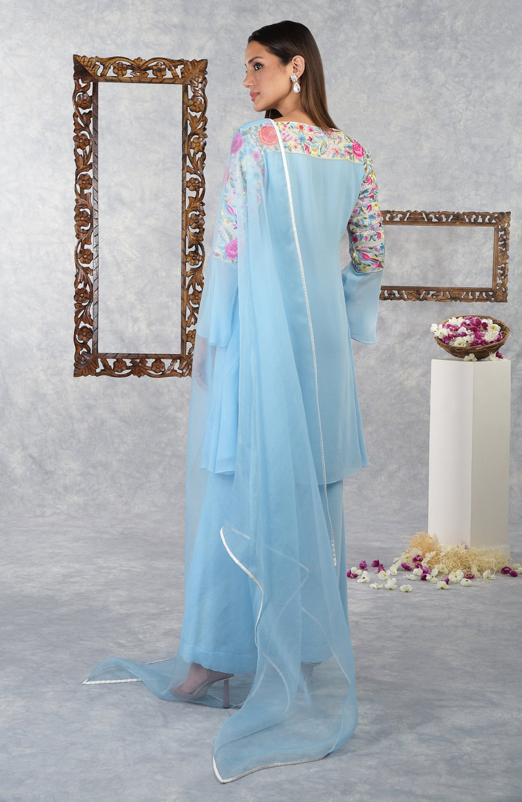 A woman models a cerulean blue Parsi Gara embroidered kurta set with a sheer dupatta.