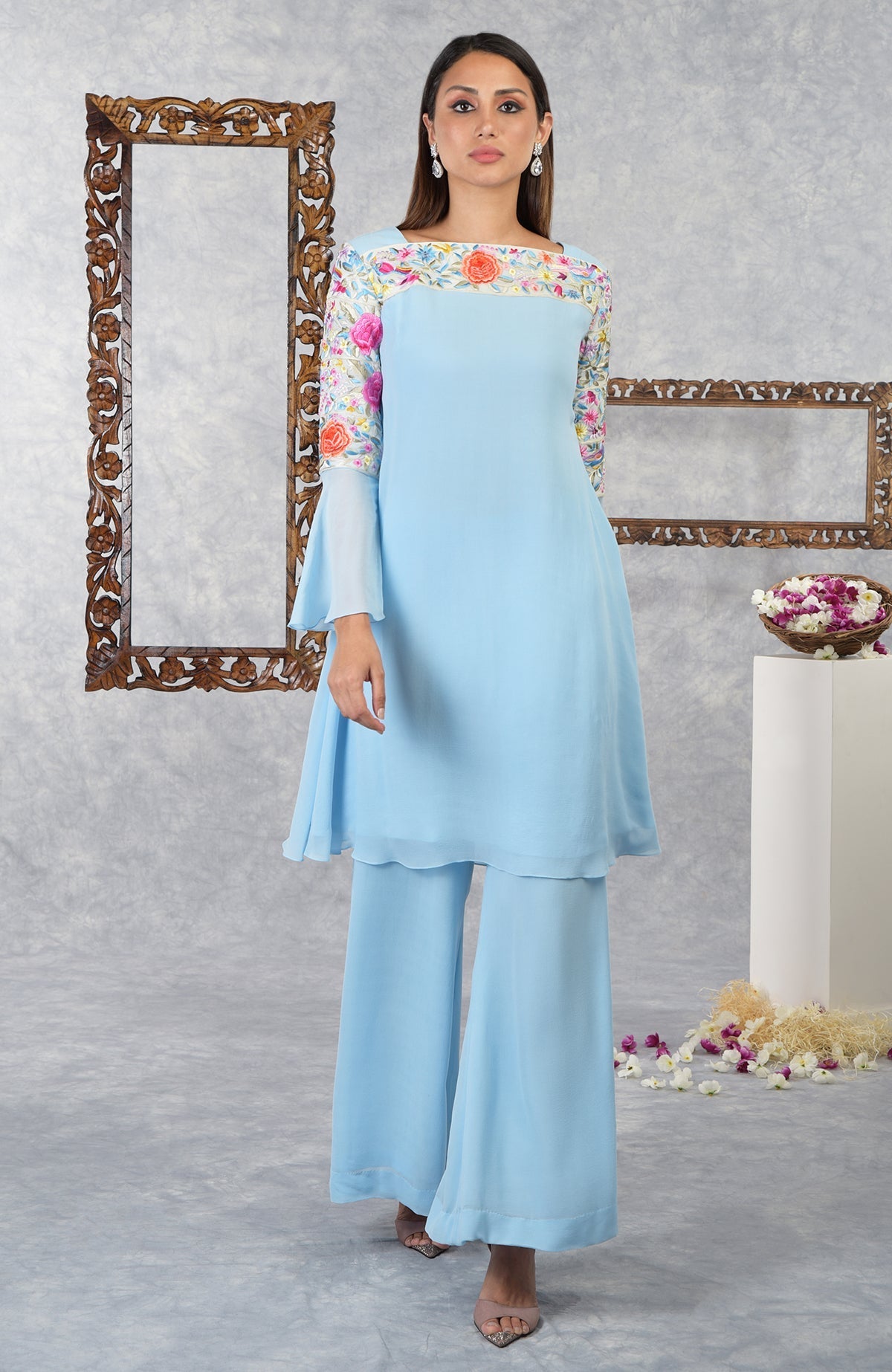 A woman models a cerulean blue Parsi Gara embroidered kurta set with bell sleeves.