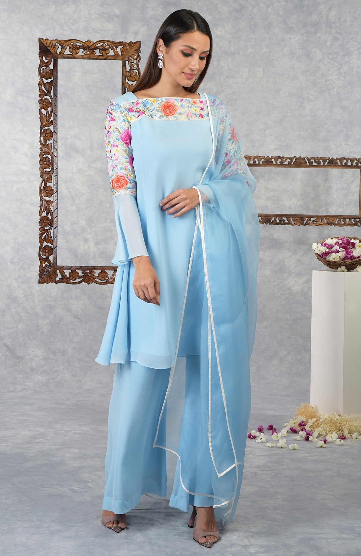 A woman models a light blue kurta set with colorful floral embroidery.