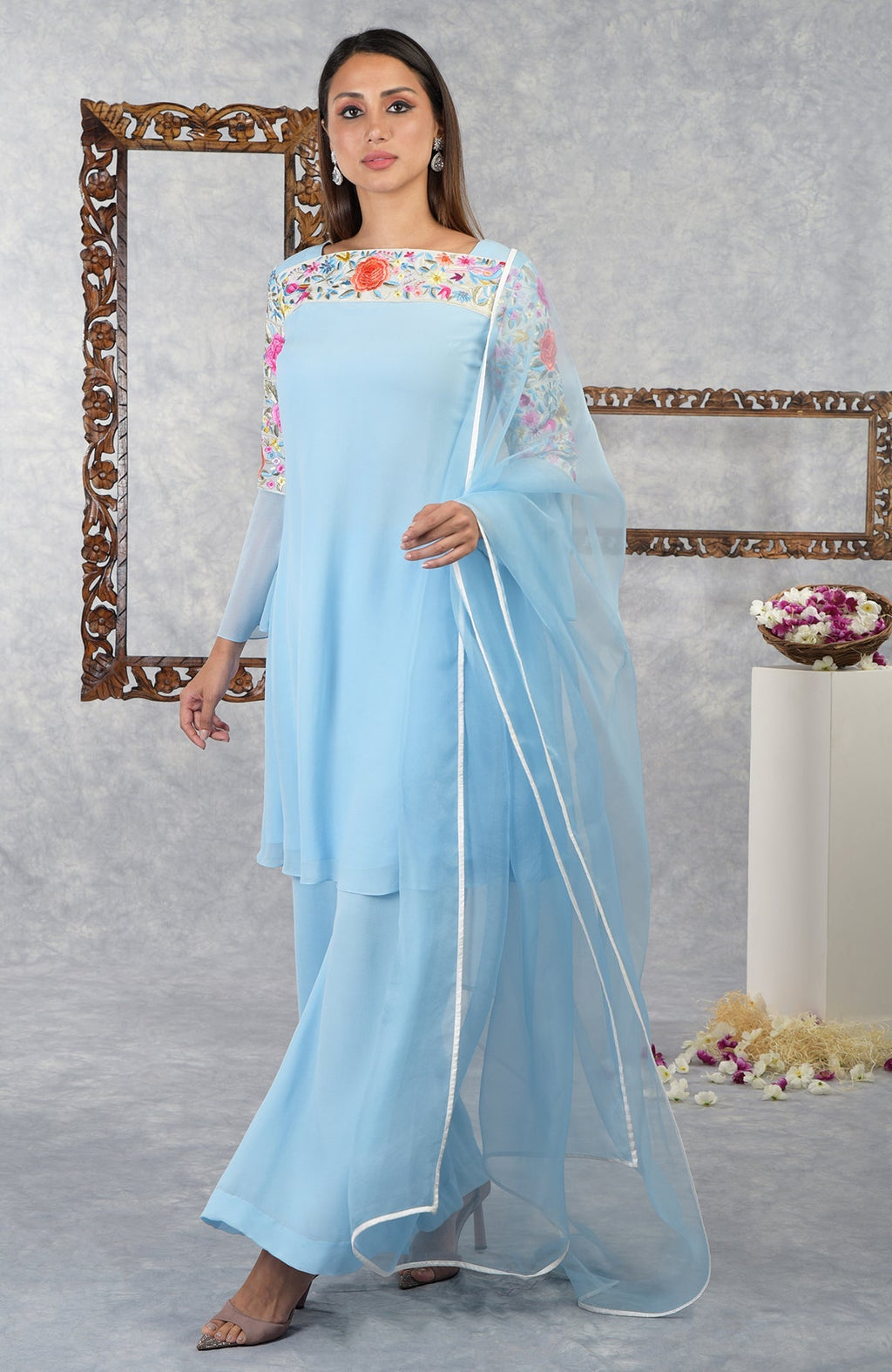 A woman models a cerulean blue Parsi Gara embroidered kurta set with a sheer dupatta.
