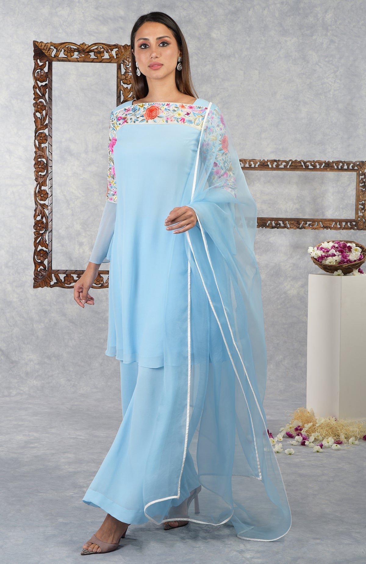 A woman models a cerulean blue Parsi Gara embroidered kurta set with a sheer dupatta.