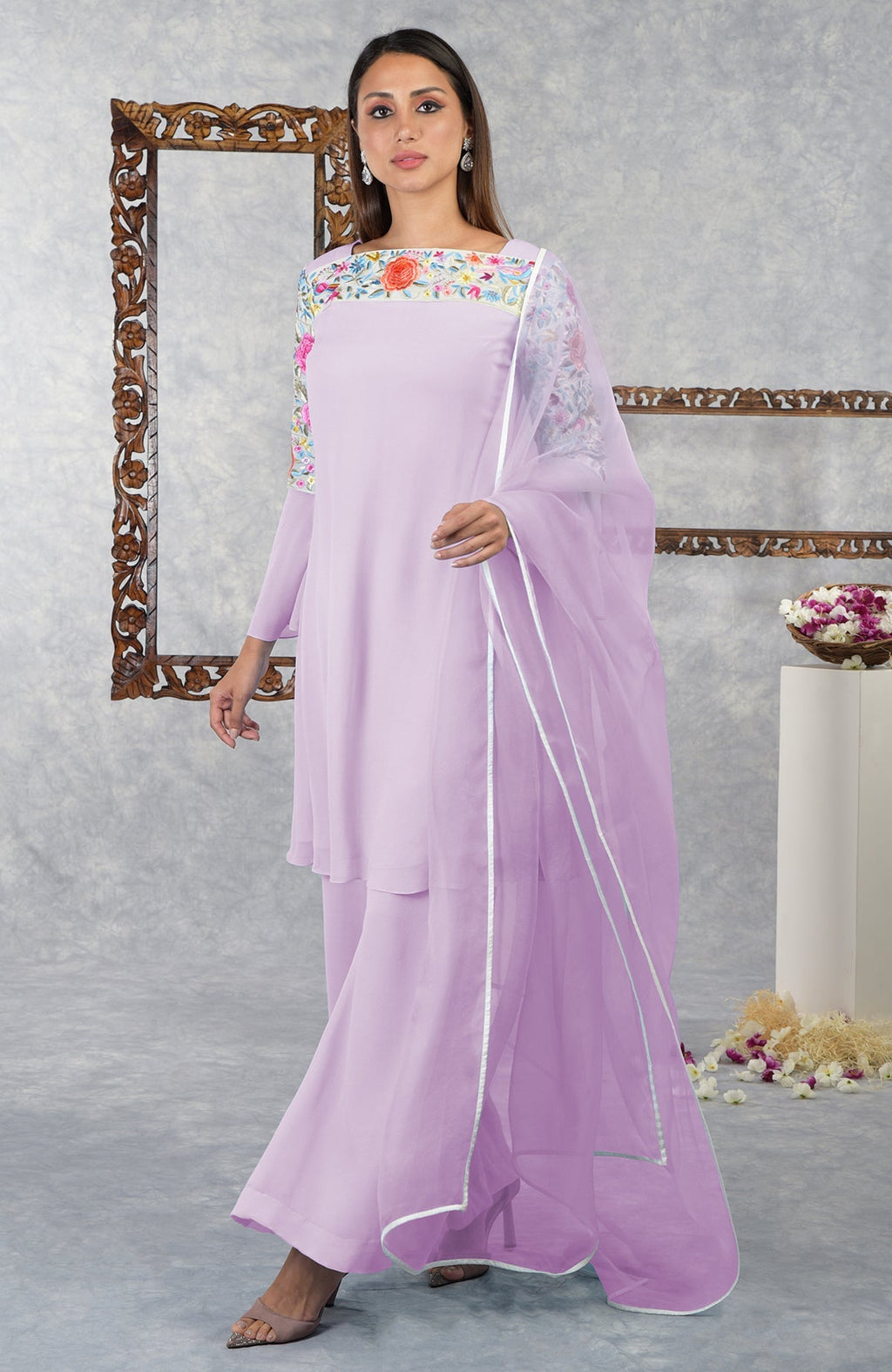 A woman models a lilac Parsi Gara embroidered kurta set with a sheer dupatta.