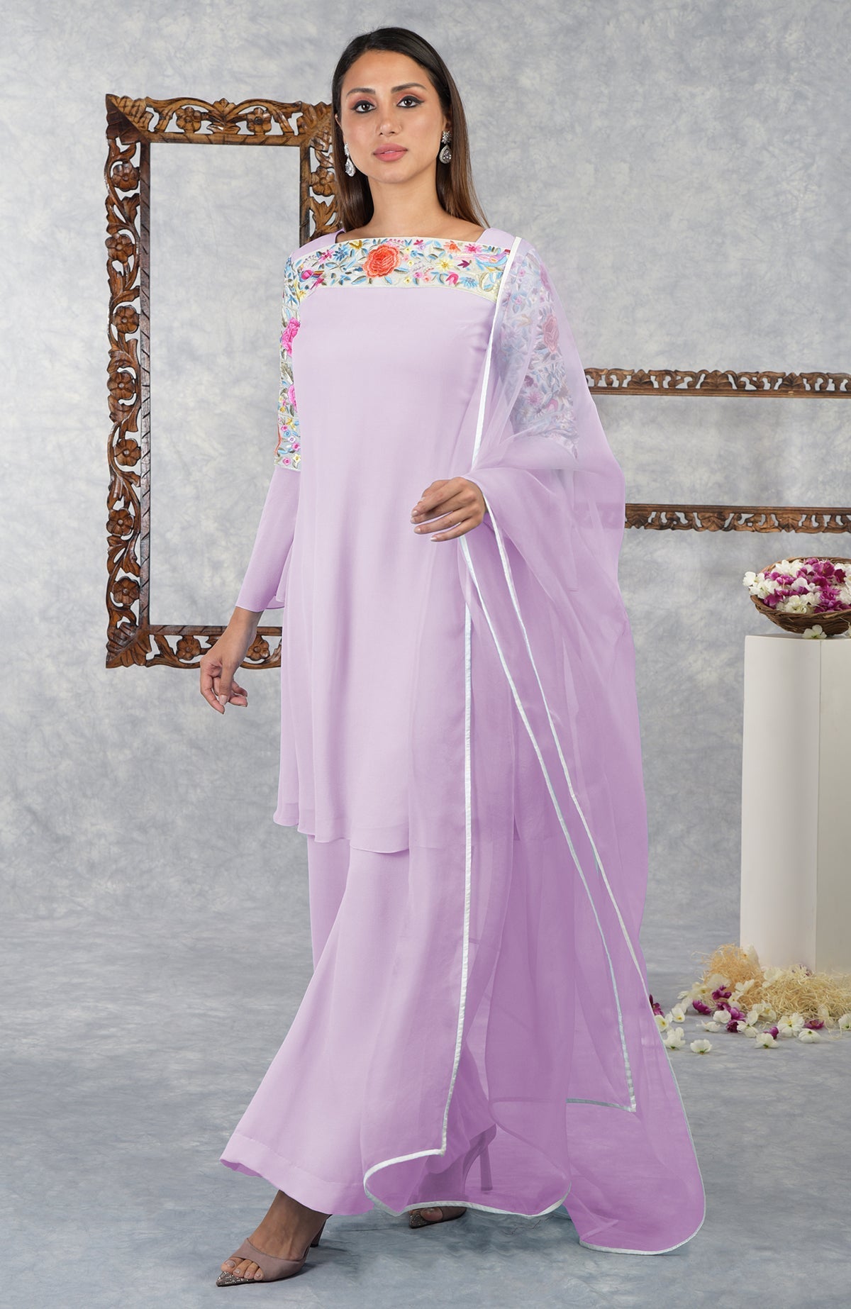 A woman models a light purple Parsi Gara embroidered kurta set with a sheer dupatta.
