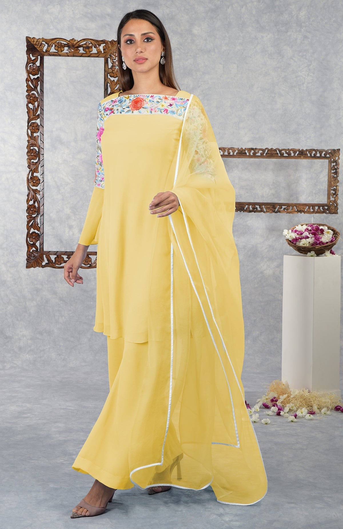A woman models a yellow Parsi Gara embroidered kurta set with a sheer dupatta.