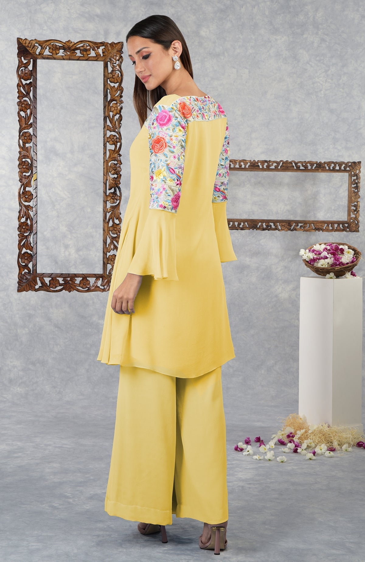 A woman models a yellow Parsi Gara embroidered kurta set with floral sleeves.